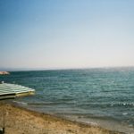 Relaxing beach view in Edremit, Türkiye, featuring a striped parasol and bright blue sea.