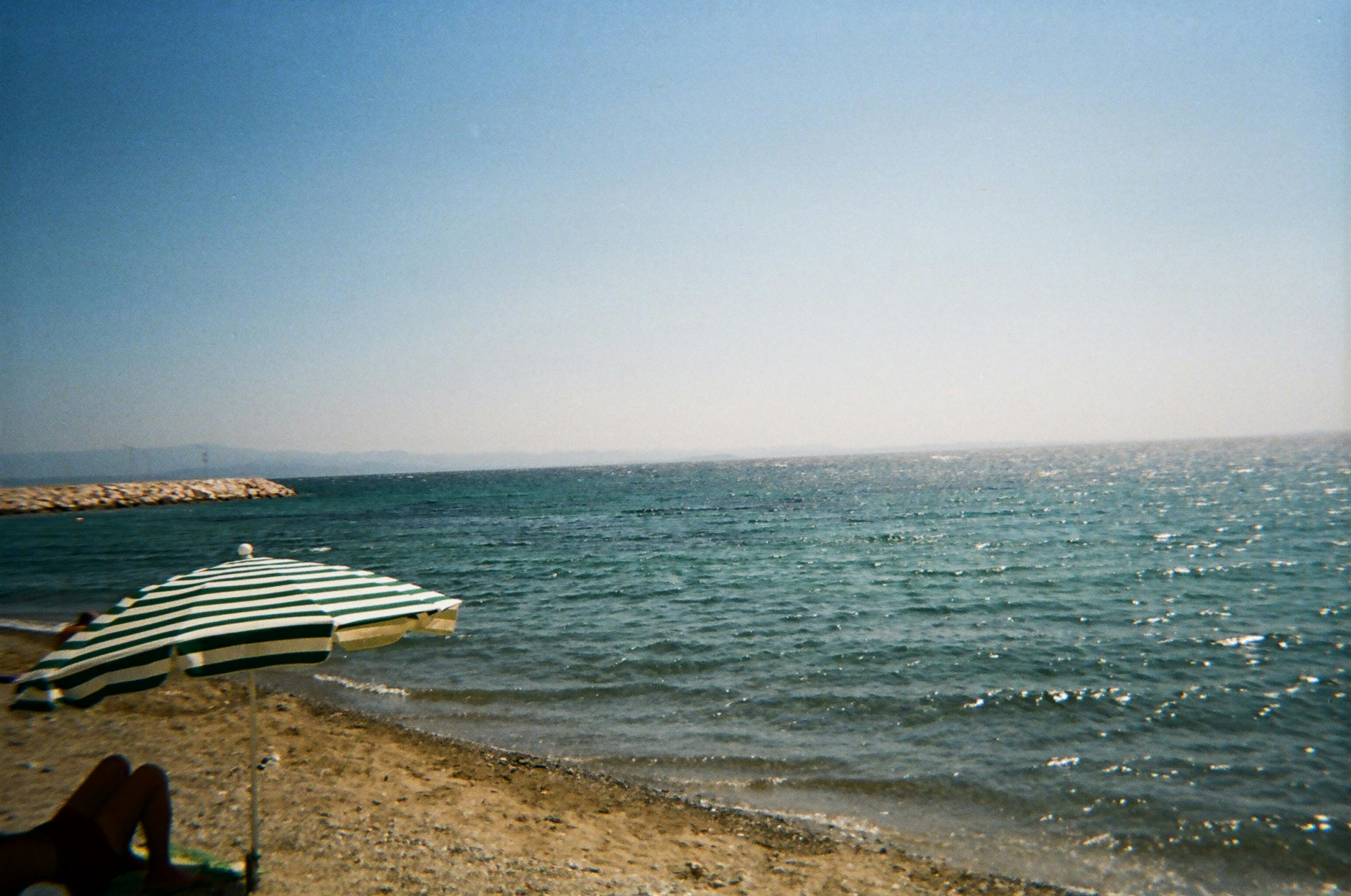 Relaxing beach view in Edremit, Türkiye, featuring a striped parasol and bright blue sea.